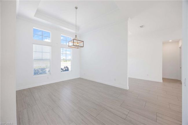 Empty room featuring light wood-type flooring, ornamental molding, baseboards, a raised ceiling, and a notable chandelier | Image 21