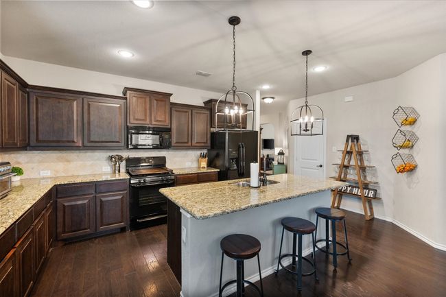 Kitchen featuring dark wood finished floors, dark brown cabinetry, black appliances, a sink, and a notable chandelier | Image 19