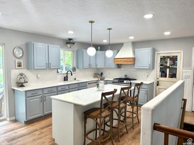 Kitchen with custom range hood, light LVP flooring, a center island, backsplash, and hanging light fixtures | Image 3