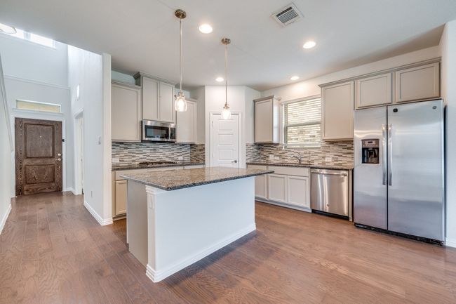 Kitchen featuring appliances with stainless steel finishes, decorative light fixtures, dark stone countertops, backsplash, and dark wood finished floors | Image 4