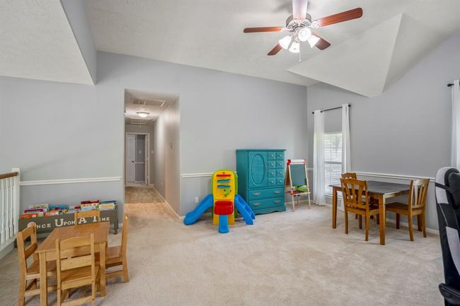 The upstairs loft-style game room offers a spacious and versatile retreat, highlighted by unique ceiling architecture with vaulted and pop-up details. Chair railing adds a polished touch, while abundant natural light makes this the perfect spot for relaxing or entertaining. | Image 23