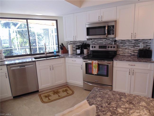 Kitchen featuring a sink, stainless steel appliances, dark stone countertops, tasteful backsplash, and white cabinetry | Image 7
