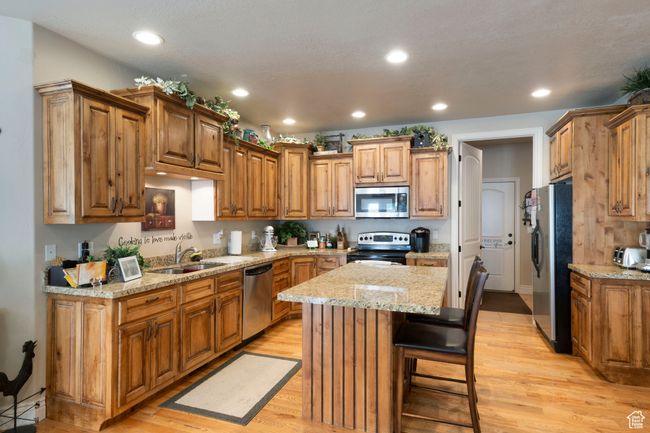Kitchen with stainless steel appliances, a kitchen island, recessed lighting, light wood-style floors, and brown cabinets | Image 10
