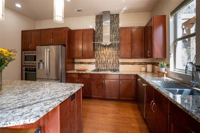 Kitchen with appliances with stainless steel finishes, wall chimney exhaust hood, plenty of natural light, light stone countertops, and recessed lighting | Image 10