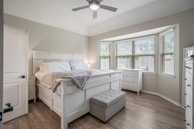 Step into your peaceful primary bedroom retreat, tucked quietly at the back of the home. Bright bay windows frame serene views of the backyard, while easy-to-maintain vinyl plank floors add a touch of warmth and comfort underfoot. A perfect spot to unwind and recharge. | Image 18