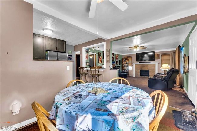 Dining area featuring a ceiling fan, dark carpet, a fireplace, and baseboards | Image 12