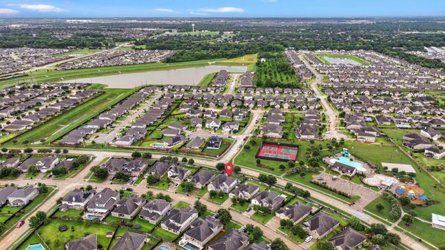 This aerial view showcases a suburban neighborhood with well-maintained homes, tree-lined streets, and nearby amenities. There's a community pool, playground, sports courts, and a scenic pond, offering a family-friendly environment. | Image 49