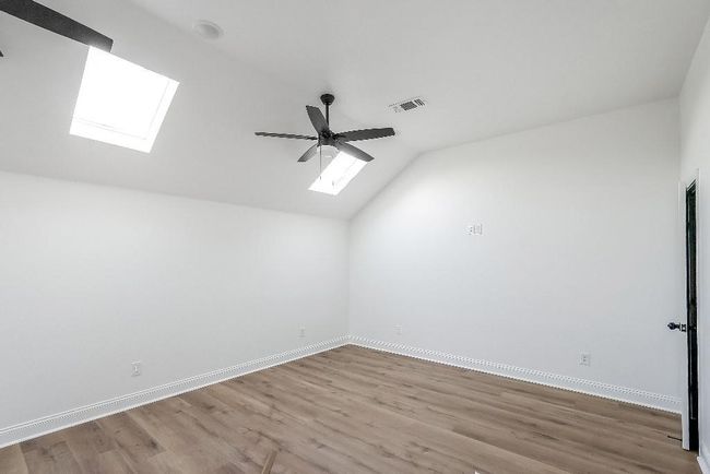 Bonus room featuring visible vents, wood finished floors, baseboards, lofted ceiling with skylight, and ceiling fan | Image 21