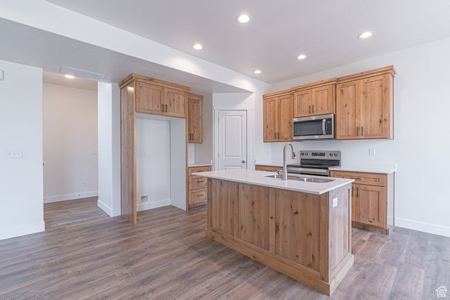 Kitchen featuring stainless steel appliances, light countertops, recessed lighting, wood finished floors, and a center island with sink | Image 5