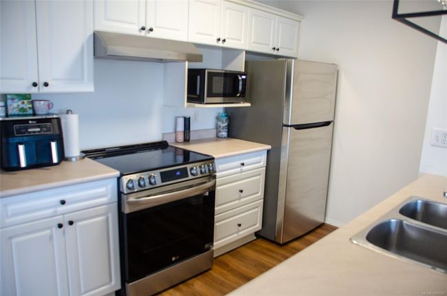 Kitchen with appliances with stainless steel finishes, under cabinet range hood, a sink, and dark wood-style flooring | Image 14