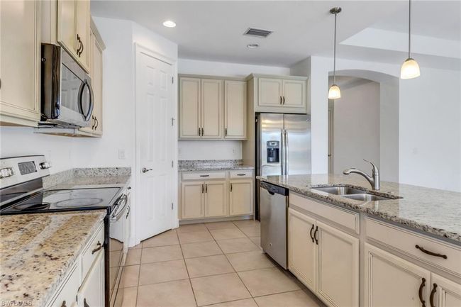 Kitchen featuring stainless steel appliances, a sink, cream cabinetry, pendant lighting, and arched walkways | Image 24
