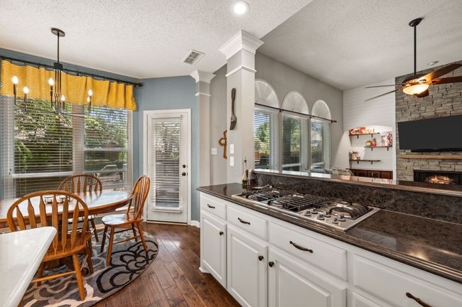Kitchen with decorative light fixtures, white cabinetry, a textured ceiling, dark wood-style flooring, and stainless steel gas stovetop | Image 14