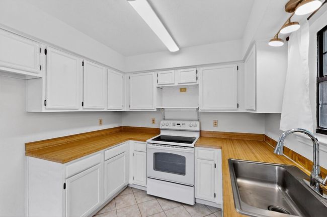 Kitchen with white electric range oven, a sink, white cabinets, light countertops, and open shelves | Image 15