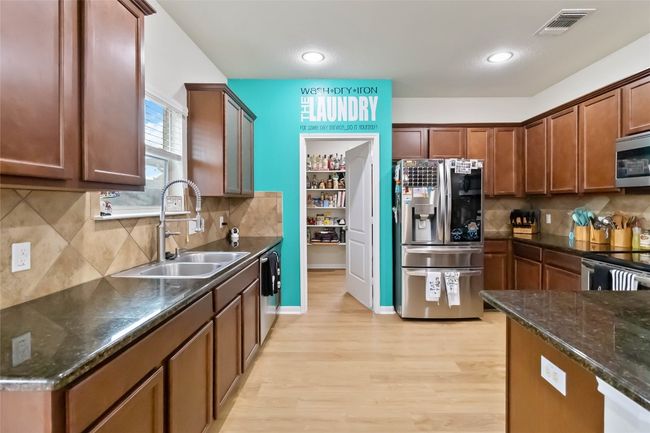 Kitchen with appliances with stainless steel finishes, light wood finished floors, tasteful backsplash, dark stone counters, and recessed lighting | Image 5