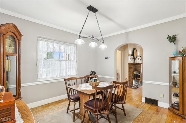 Dining room with a stone fireplace, visible vents, arched walkways, crown molding, and light wood-style flooring | Image 8