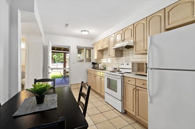 Kitchen with light brown cabinets, under cabinet range hood, backsplash, white appliances, and light tile patterned floors | Image 26