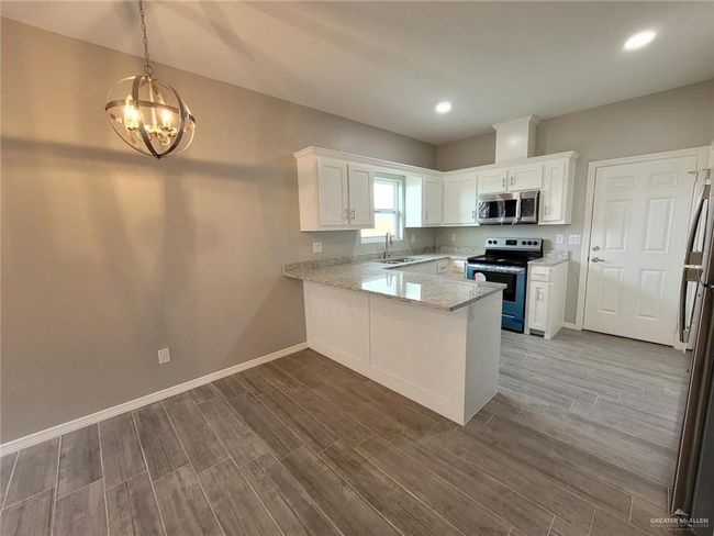 Kitchen featuring stainless steel appliances, a peninsula, a sink, a notable chandelier, and wood finished floors | Image 18