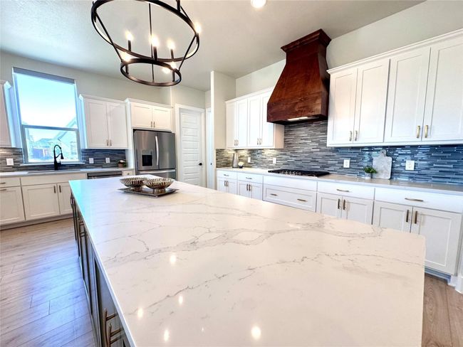Kitchen featuring stainless steel appliances, custom exhaust hood, a kitchen island, a chandelier, and white cabinets | Image 8