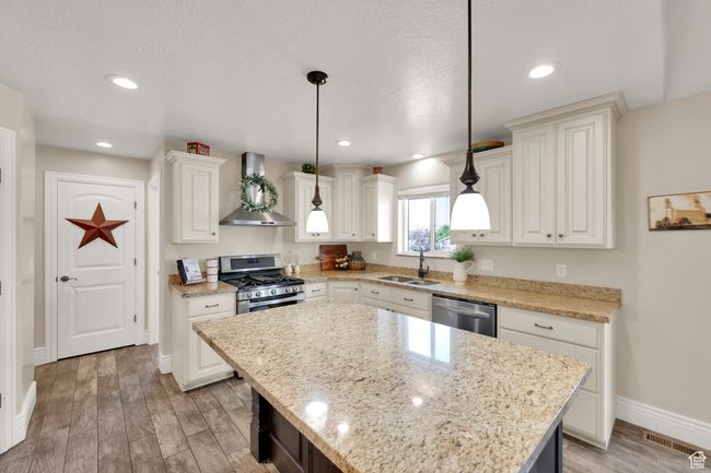 Kitchen featuring wall chimney exhaust hood, stainless steel appliances, light wood-type flooring, hanging light fixtures, and white cabinetry | Image 7