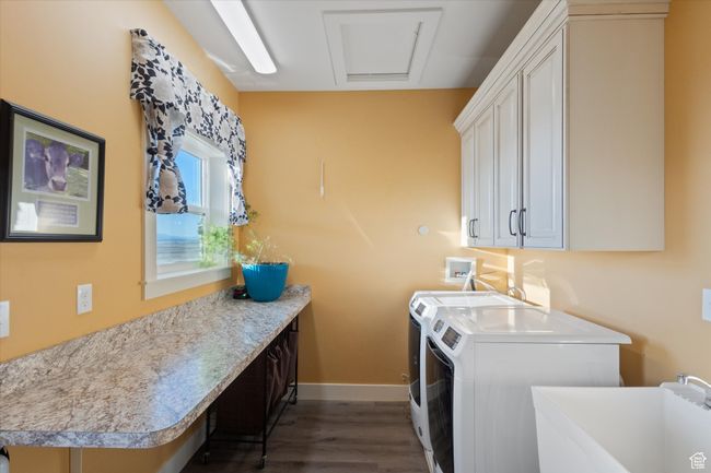 Clothes washing area featuring dark wood-style floors, baseboards, washing machine and clothes dryer, cabinet space, and a sink | Image 24