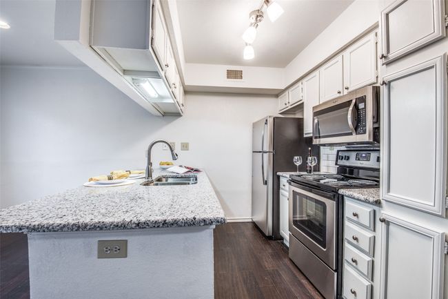 Kitchen featuring stainless steel appliances, a sink, a peninsula, dark wood finished floors, and white cabinetry | Image 4