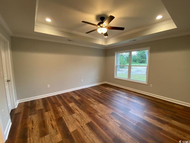 Spare room featuring a raised ceiling, dark wood-style flooring, crown molding, ceiling fan, and baseboards | Image 5