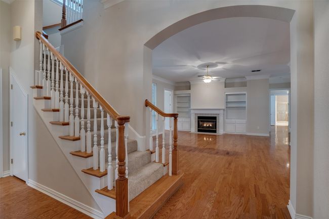 Stairway featuring ceiling fan, wood finished floors, built in shelves, arched walkways, and a fireplace | Image 26