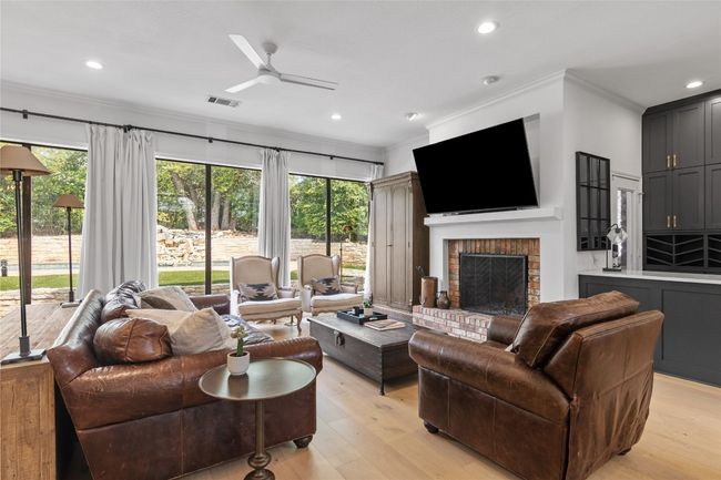 Living area with light wood-type flooring, visible vents, a ceiling fan, a brick fireplace, and crown molding | Image 12