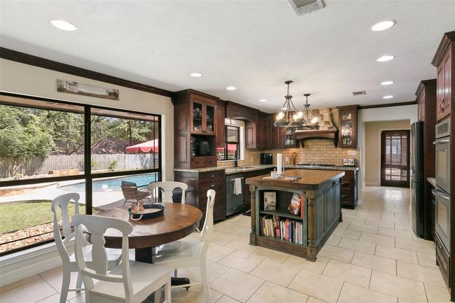 This spacious kitchen features elegant wooden cabinetry, a central island with bookshelves, and modern appliances. Large windows offer a view of the backyard pool, creating a bright and inviting atmosphere. | Image 16