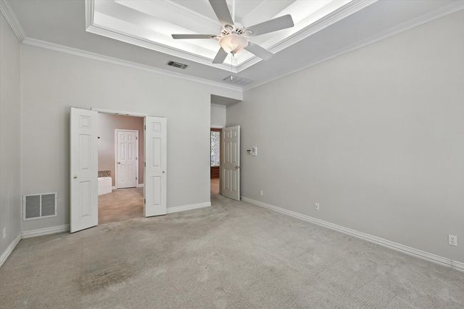 Unfurnished bedroom featuring light colored carpet, ornamental molding, a raised ceiling, and a ceiling fan | Image 12