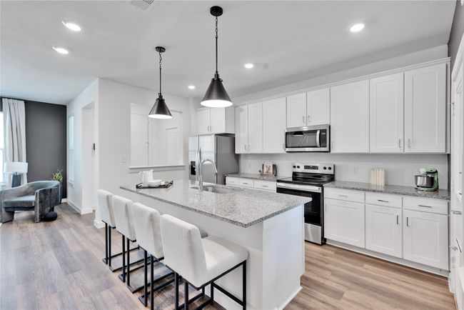 Kitchen featuring stainless steel appliances, a sink, white cabinets, light wood-style floors, and a center island with sink | Image 11