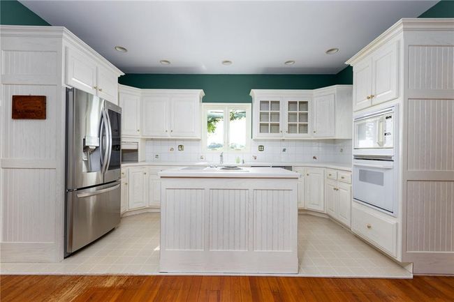 Kitchen featuring white cabinetry, white appliances, light wood-type flooring, a center island, and decorative backsplash | Image 40