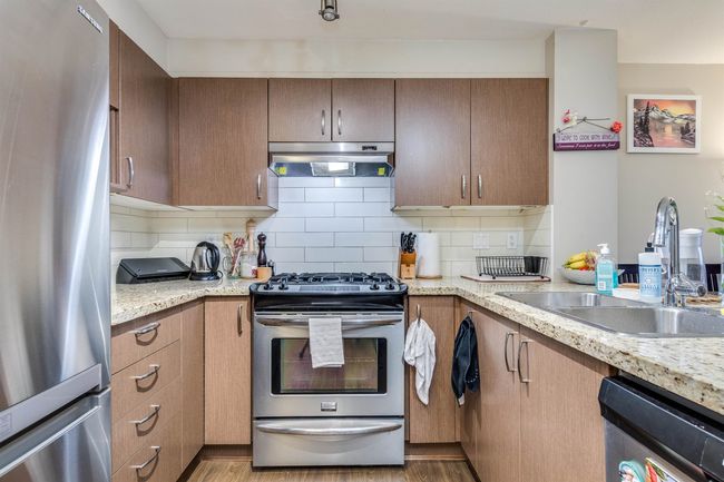 Kitchen featuring backsplash, a sink, light wood-type flooring, under cabinet range hood, and stainless steel appliances | Image 6