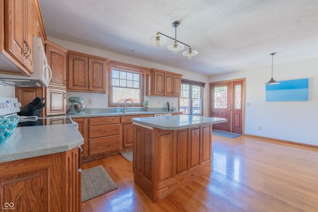 kitchen with a center island, brown cabinetry, light wood finished floors, light countertops, and decorative light fixtures | Image 11