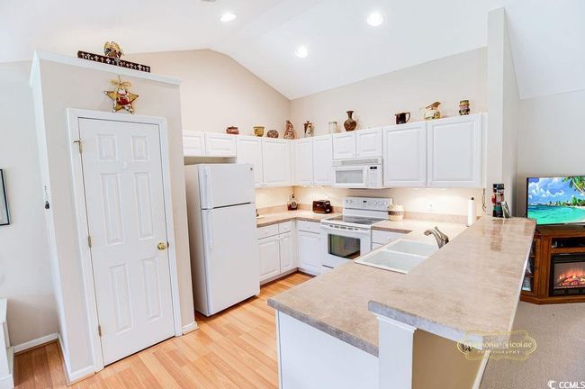 Kitchen featuring white appliances, a peninsula, lofted ceiling, light wood-style floors, and light countertops | Image 8