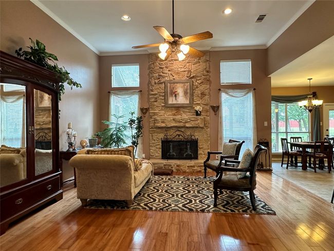 Living area with ornamental molding, ceiling fan with notable chandelier, light wood finished floors, visible vents, and a stone fireplace | Image 7