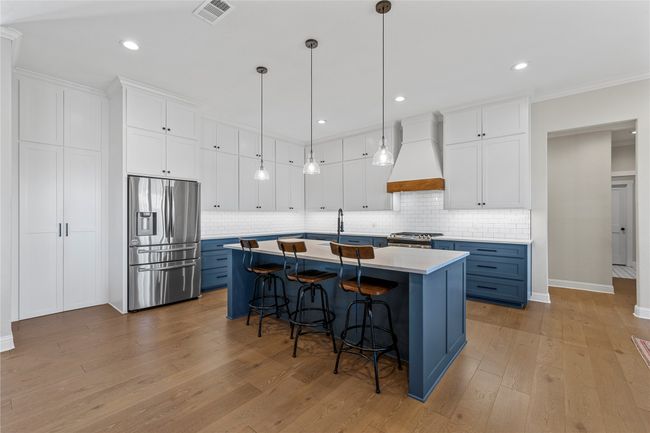 Kitchen with a kitchen breakfast bar, visible vents, custom exhaust hood, blue cabinets, and stainless steel appliances | Image 10