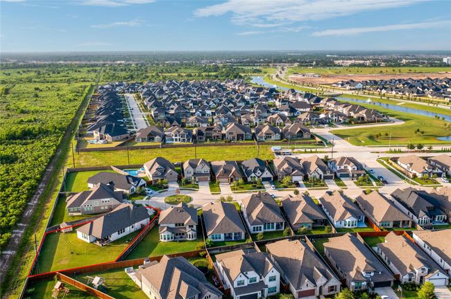 This aerial photo showcases a suburban neighborhood with well-maintained homes on spacious lots, set against a backdrop of green space and clear skies. The orderly streets and nearby natural areas create an inviting residential environment. | Image 49