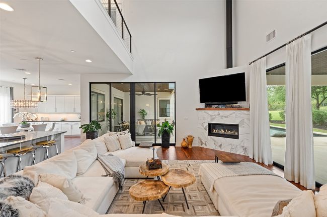Centered by a modern gas fireplace, this spacious living room flows into the kitchen as well as to both covered patios. | Image 5