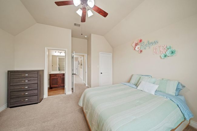 This bedroom features a vaulted ceiling, neutral walls, ceiling fan, and carpeted flooring. The room connects to a bathroom and has hallway access. | Image 29