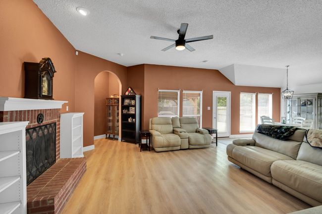 Living room with arched walkways, a textured ceiling, ceiling fan, light wood finished floors, and a brick fireplace | Image 8
