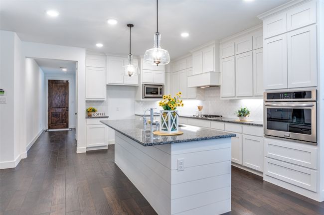 Kitchen with a center island with sink, stainless steel appliances, hanging light fixtures, white cabinetry, and granite counters | Image 4