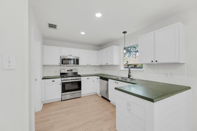 Kitchen with stainless steel appliances, visible vents, a sink, and dark countertops | Image 9