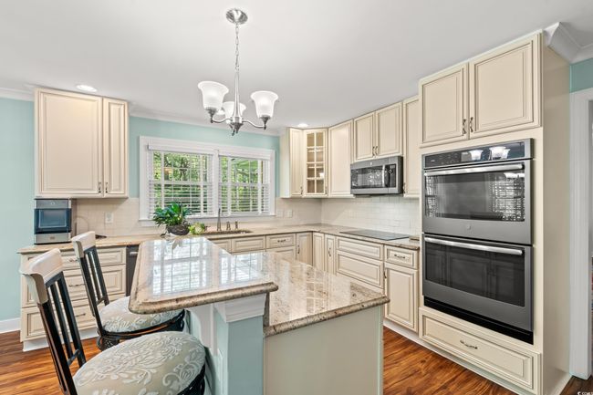 Kitchen featuring appliances with stainless steel finishes, cream cabinets, a chandelier, light stone countertops, and dark wood-style floors | Image 5