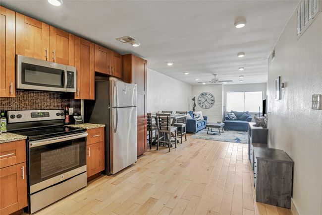 Kitchen featuring appliances with stainless steel finishes, light wood finished floors, a ceiling fan, light stone countertops, and backsplash | Image 14