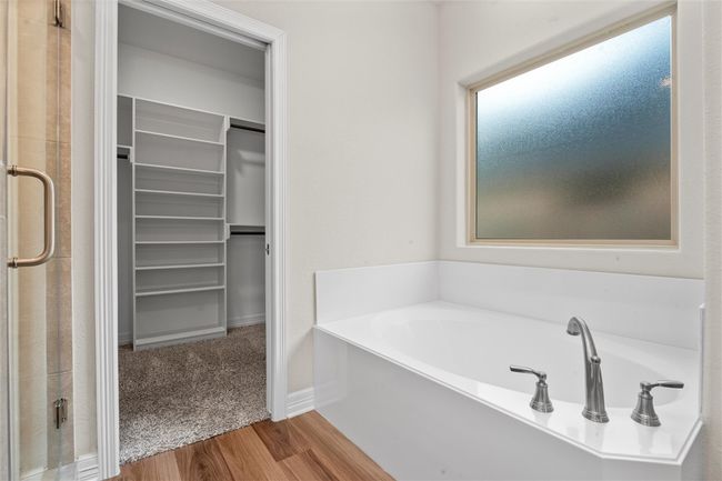 Full bath with a walk in closet, a bath, a stall shower, wood finished floors, and baseboards | Image 21