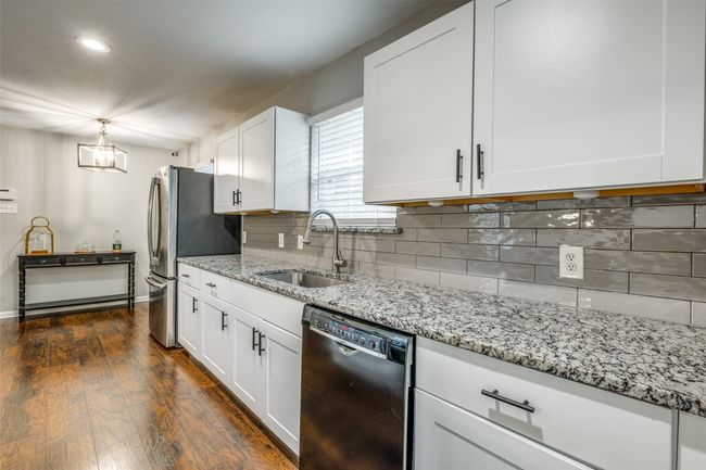 Kitchen with black dishwasher, white cabinets, dark wood-style flooring, freestanding refrigerator, and light stone countertops | Image 22