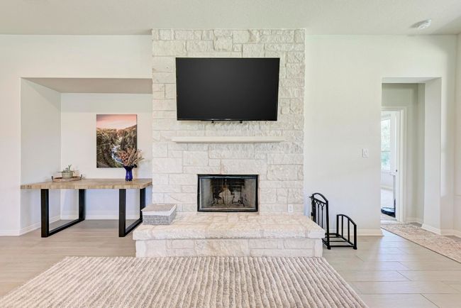 An impressive white stone, wood-burning fireplace with raised hearth also features a hydraulic TV mount that makes adjusting the television easy (mount conveys). | Image 8