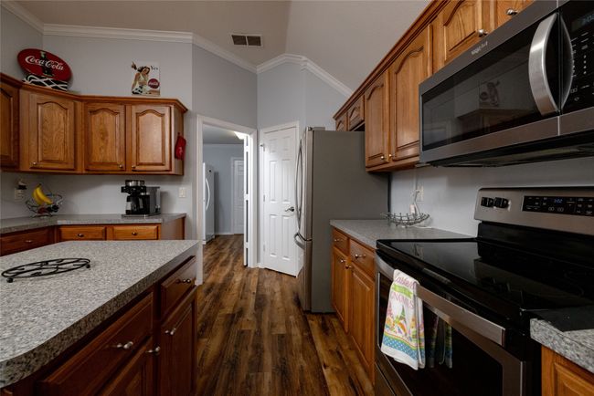Kitchen featuring dark wood-style floors, visible vents, appliances with stainless steel finishes, brown cabinetry, and ornamental molding | Image 19
