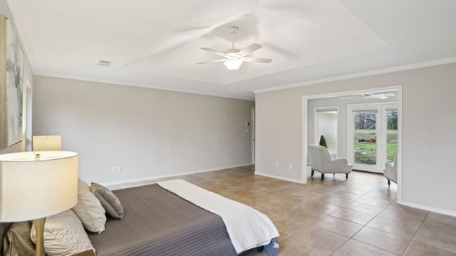 Bedroom with light tile patterned floors, crown molding, visible vents, baseboards, and a tray ceiling | Image 25